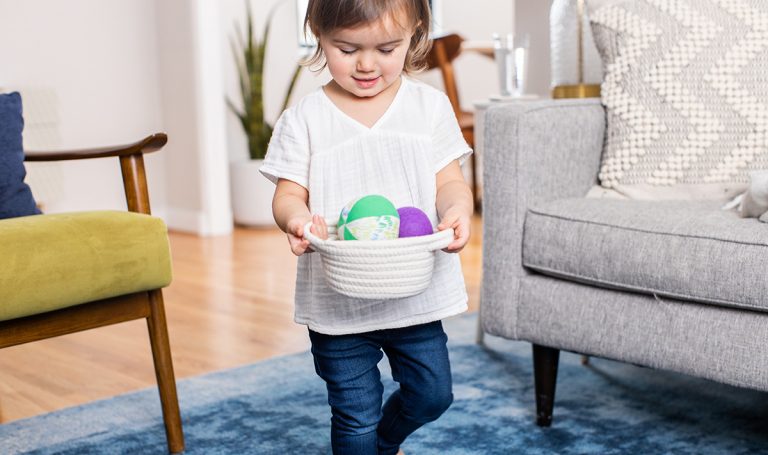 Young child carrying a basket filled with colorful balls