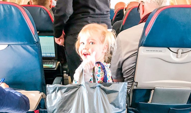 Young child walking down the aisle of an air plane holding a grey bag