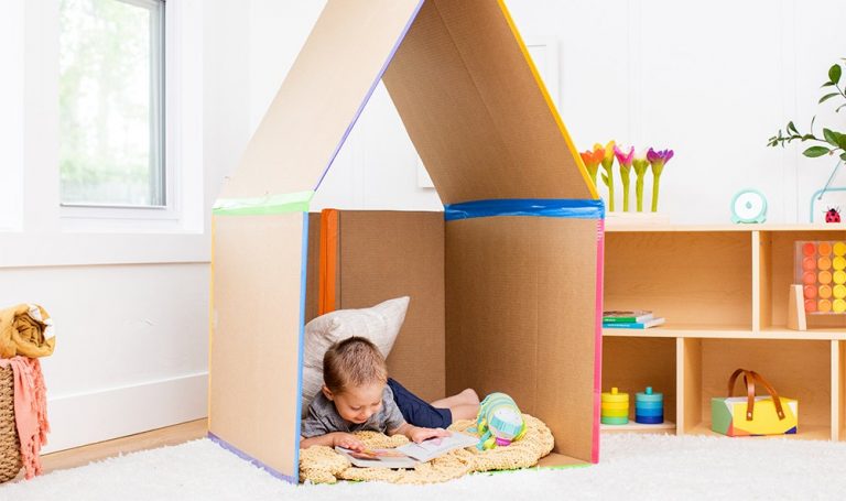 Toddler sitting in a cardboard box reading on a blanket