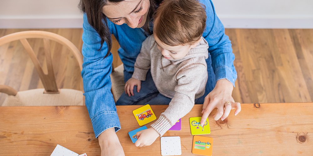 Toddler sitting on a woman's lap looking at the Memory Game cards by Lovevery