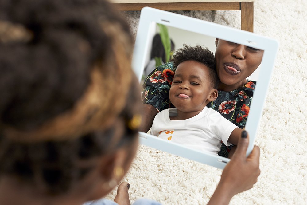 Young child sitting on a woman's lap while they look in a mirror sticking out their tongues