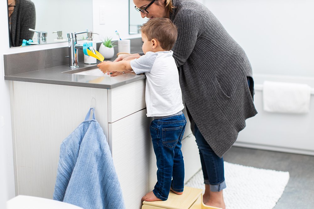 Toddler standing on a stool washing his hands at the bathroom sink