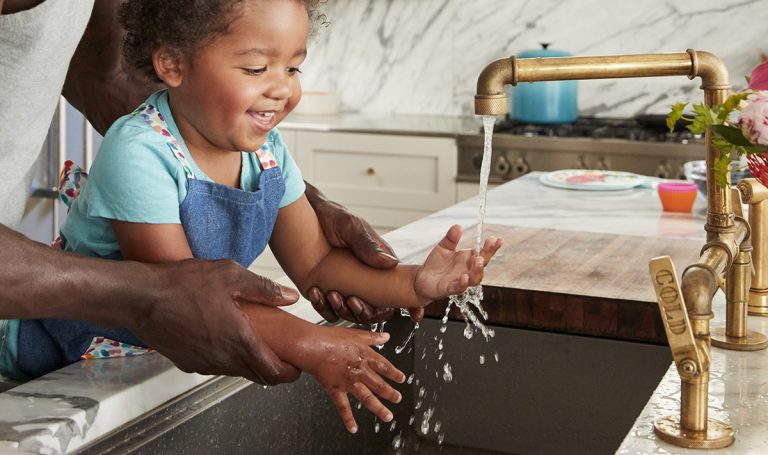 Toddler playing with water coming from the kitchen sink