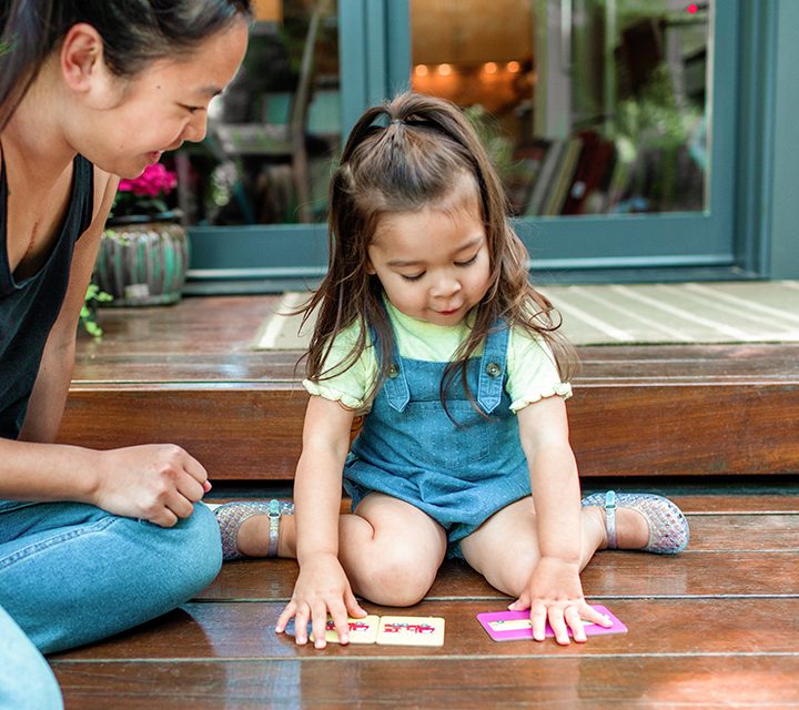 Toddler sitting on the ground outside playing with the Memory Game cards by Lovevery
